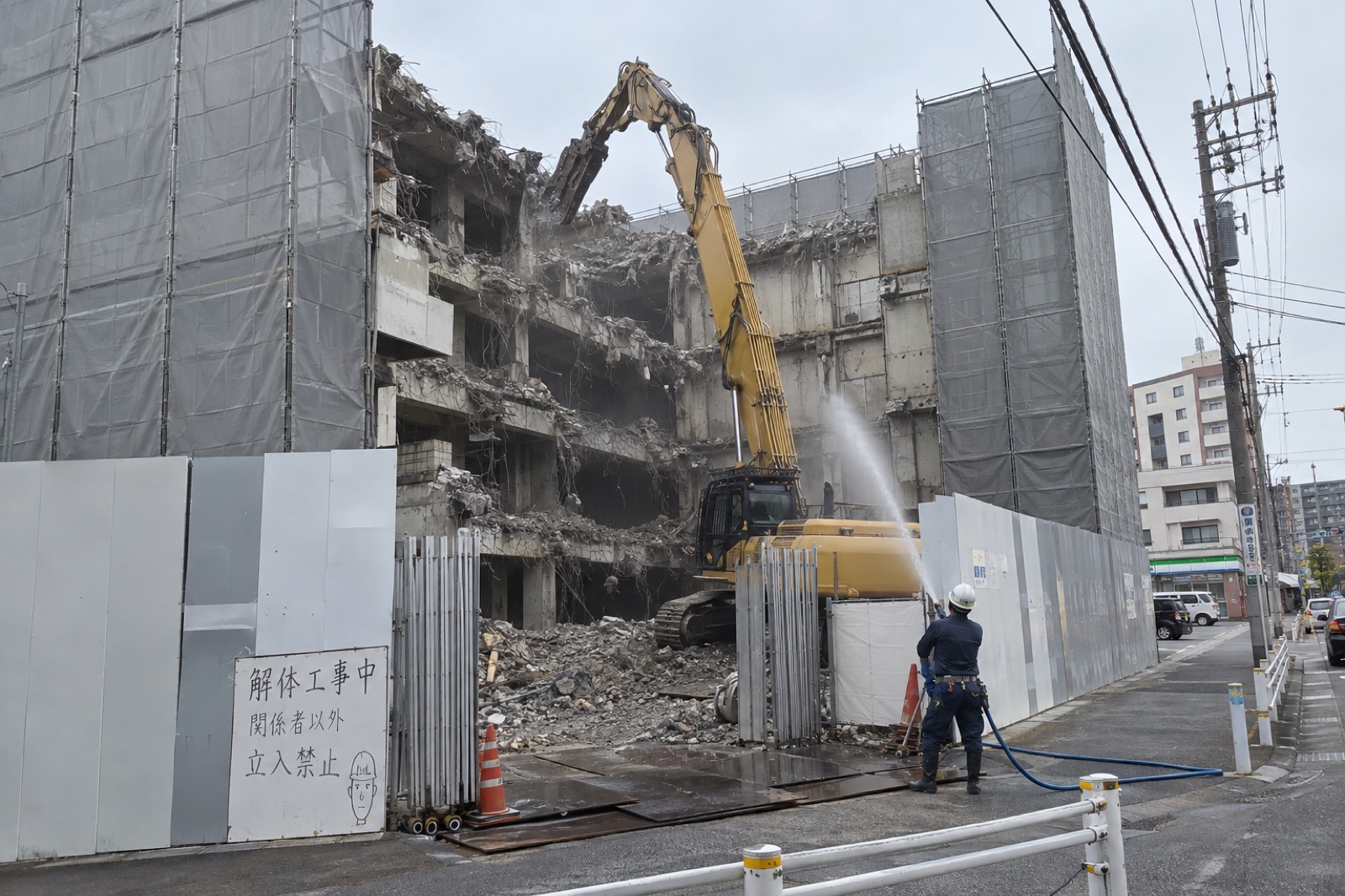 養生パネルで囲った建物の解体現場で散水しながら作業する様子